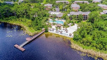 An aerial view of a resort with a swimming pool, a dock, and lush greenery.