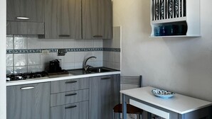 A compact kitchen with grey cabinets, a white countertop, a gas stove, and a small dining table with a bowl.