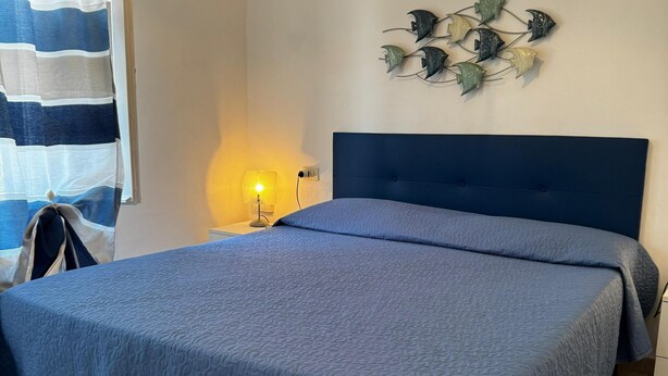 A bedroom with a large bed, a nightstand with a lamp, a striped curtain, and a wall-mounted plant decoration.
