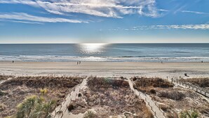 A beach with a clear sky, ocean, and a sandy path leading to the water.