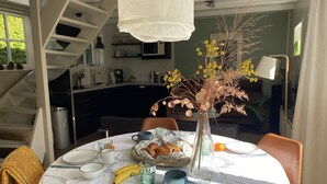 A dining table set with plates, cups, and a vase of flowers. A staircase and kitchen are visible in the background.