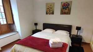 Un dormitorio con cama, dos mesitas de noche, una manta roja y dos cuadros colgados en la pared.