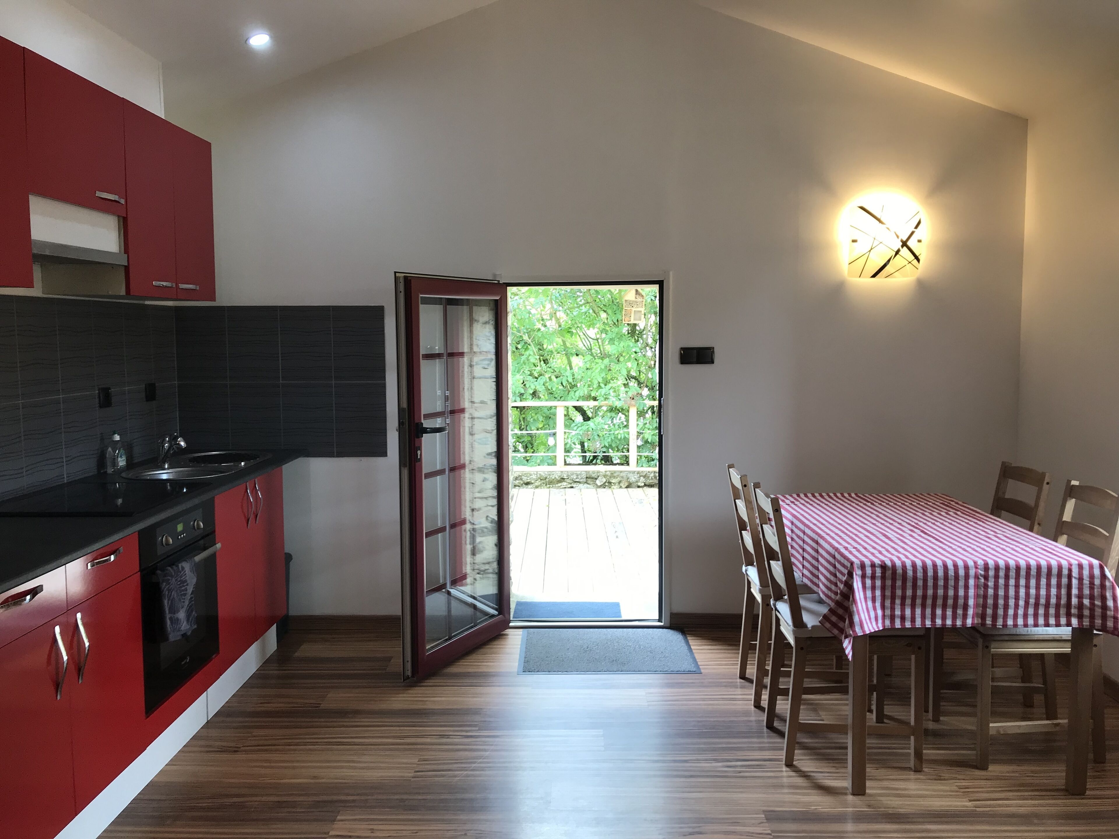 Une cuisine moderne avec des meubles rouges, un plan de travail noir et une table à manger en bois recouverte d’une nappe à carreaux.