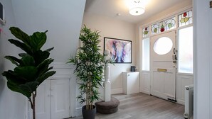 Un interior moderno con una planta grande en maceta, una obra de arte enmarco y una puerta blanca con vidrieras.