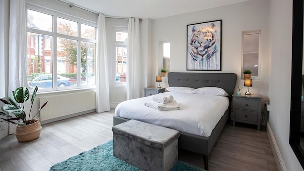 Un dormitorio moderno con una cama grande, mesitas de noche, una ventana con cortinas, un cuadro y vistas al exterior.