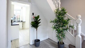 Un pasillo con una escalera, una planta en maceta y vista a una cocina.