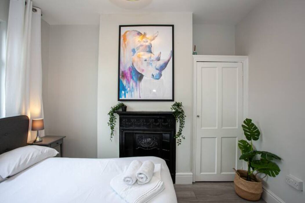 A hotel room with a bed, a framed abstract painting, a fireplace, and a potted plant.