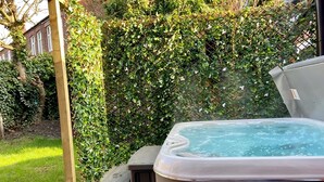 Un jacuzzi en una terraza de madera con una cerca de malla y follaje al fondo.