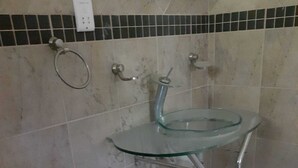 Ein Badezimmer mit einem Waschbecken aus Glas, einer Toilette und gefliesten Wänden.