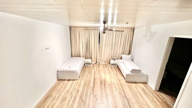 Une chambre avec deux lits simples, un ventilateur de plafond et un plancher en bois.