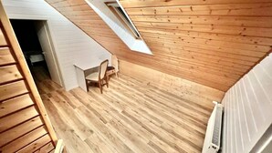 Un plafond en pente avec un puits de lumière, un plancher en bois, une chaise et un radiateur.