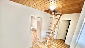 Une pièce avec un plancher en bois, un escalier en bois et des murs blancs.