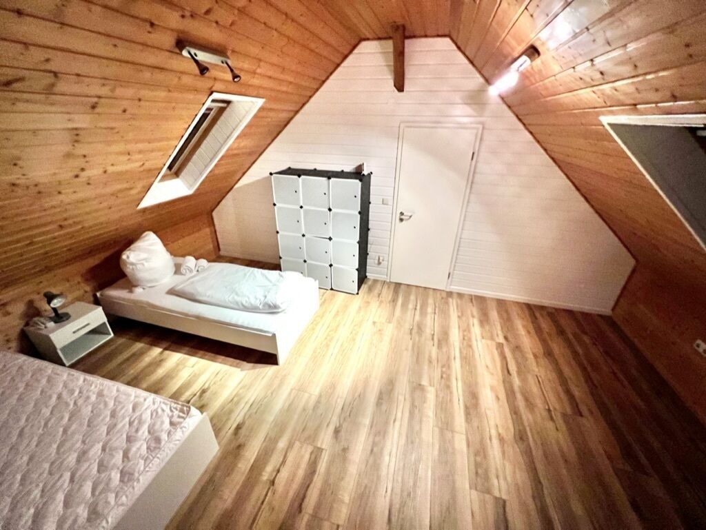 A small, sloped-roofed attic bedroom with a bed, a white wardrobe, and a window.