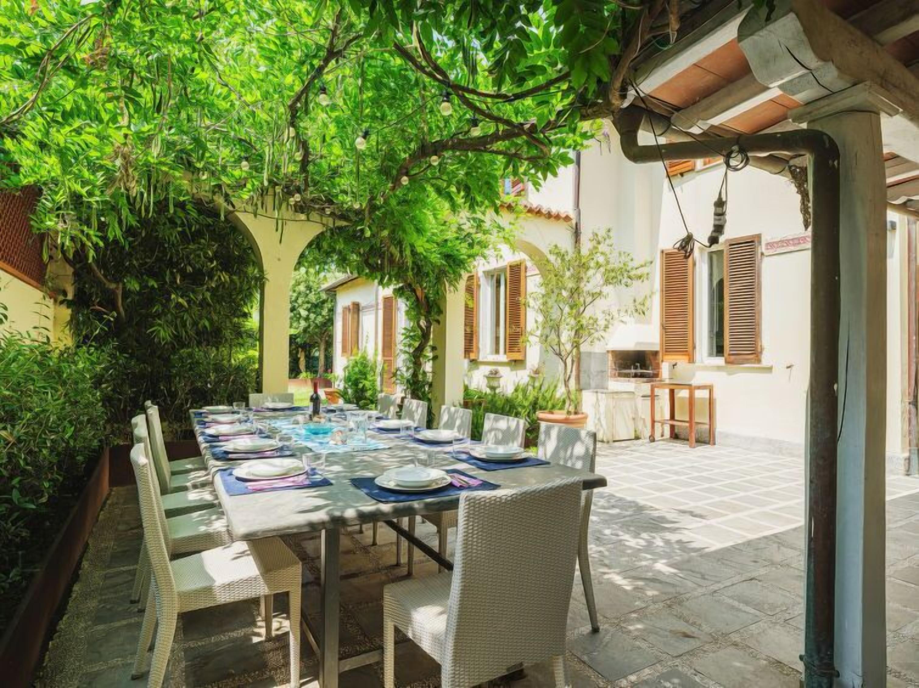 An outdoor dining area with a table set for four, surrounded by greenery and a building with traditional architecture.