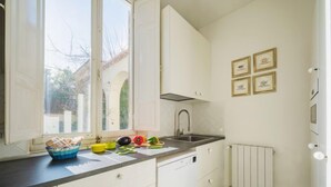 Eine kleine Küche mit weißen Schränken, einer schwarzen Arbeitsplatte und einem Fenster mit Blick auf ein Gebäude und Bäume.