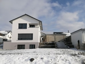 Een modern huis met twee verdiepingen, een plat dak, grote ramen en een zichtbare trap naar de ingang.