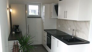 A modern kitchen with white cabinets, a black countertop, and a built-in oven. There is a potted plant and a window providing natural light.