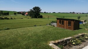 A rural landscape with a small wooden building, a large tree, and rolling green fields.
