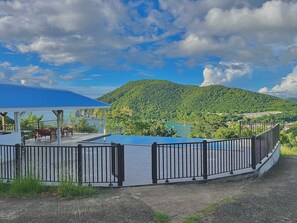 Un espace extérieur abrité comprenant une piscine, une terrasse entourée d’une clôture et offrant une vue sur un lac et des montagnes.