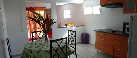 A kitchen with orange cabinets, a dining table with a floral tablecloth, and a purple trash bin.