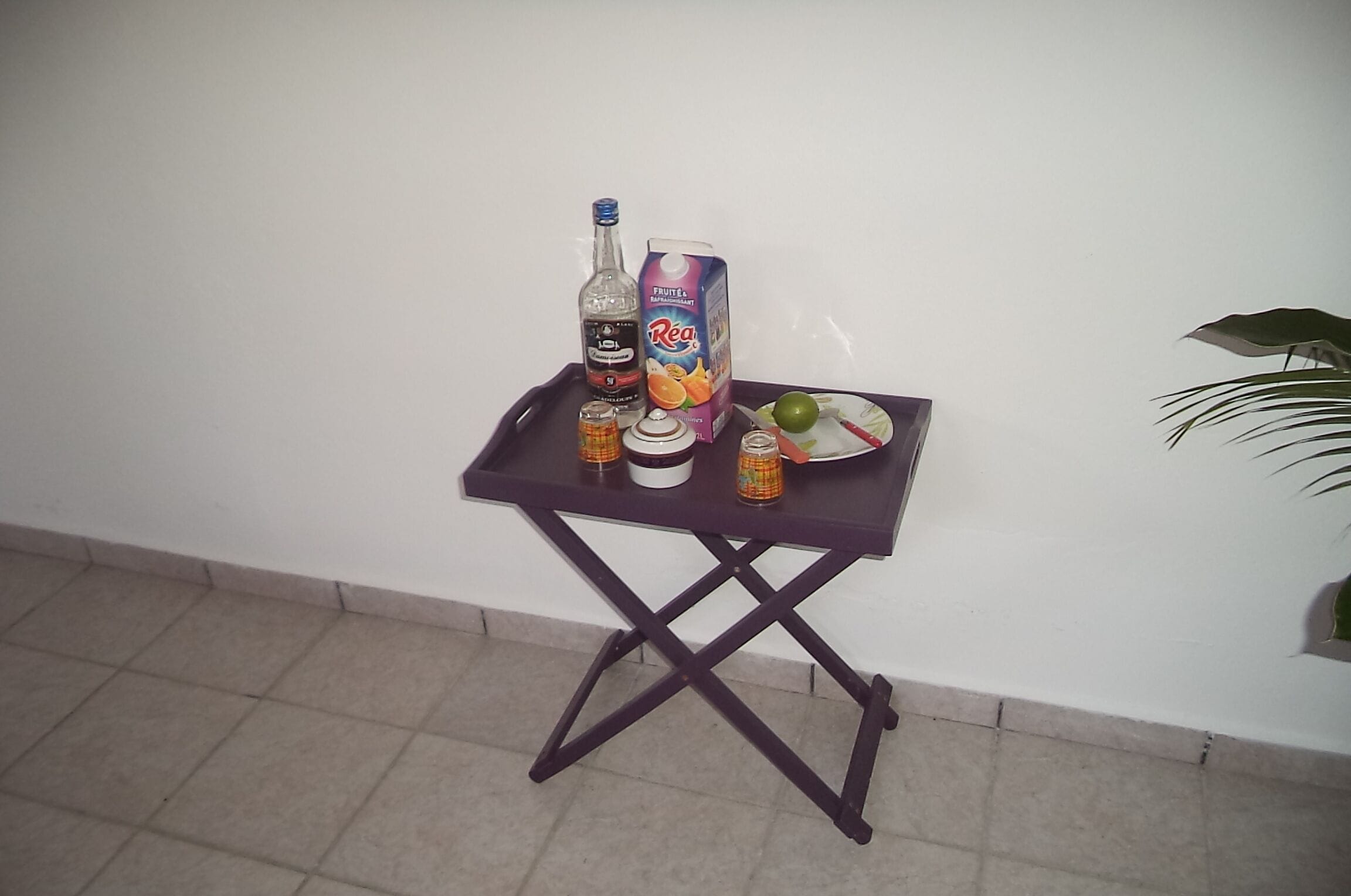 Ein kleiner Tisch mit einer Packung Fruchtsaft, einer Flasche Alkohol, einem Glas und einem Teller mit einer grünen Frucht.