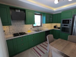 A compact kitchen with green cabinets, a gas stove, a sink, and a microwave.