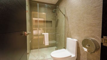 Uma casa de banho moderna com cabine de duche em vidro, sanita branca e suporte para toalhas.