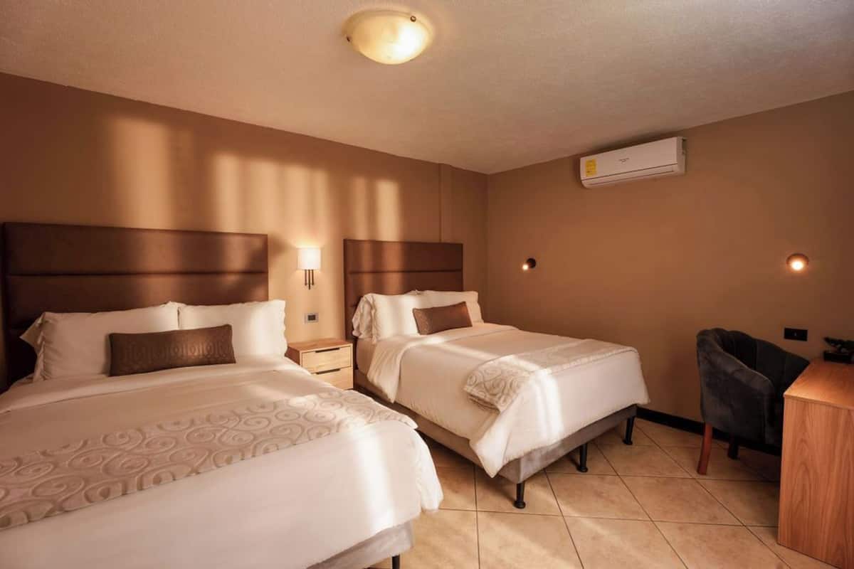 Quarto de hotel com duas camas, uma mesa, uma cadeira e ar condicionado.