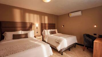Quarto de hotel com duas camas, uma mesa, uma cadeira e ar condicionado.