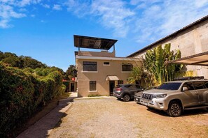 A two-story building with a solar panel on the roof, parked cars, and a gravel driveway. - L'Aurora Inn Hostel  (Guatemala City)
