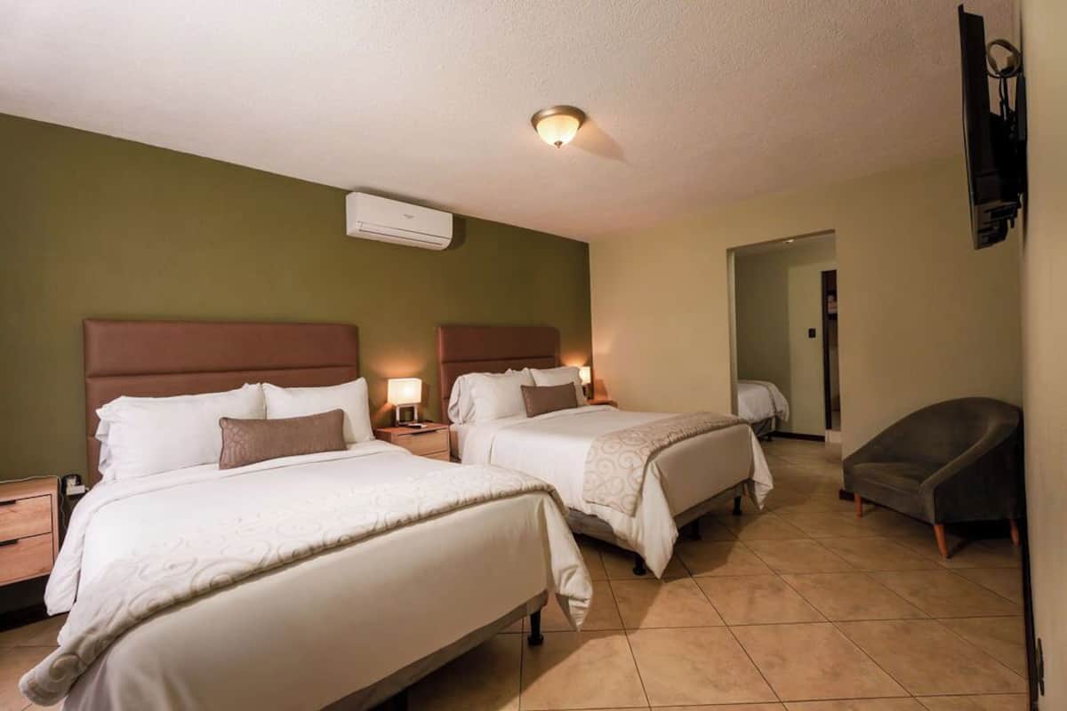 Quarto de hotel com duas camas, uma cadeira, uma TV e um ar condicionado.