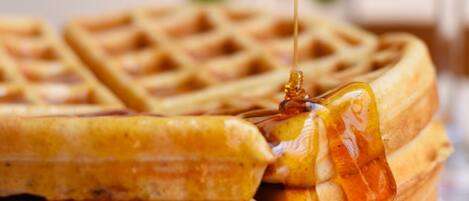 A close-up of a waffle with syrup being poured over it.