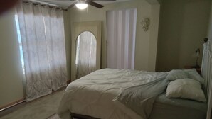 Ein Schlafzimmer mit Bett, Deckenventilator, Fenster mit Vorhängen und einer Tür.