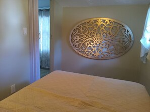 Une chambre à coucher comprenant un lit, un panneau décoratif fixé au mur et une porte donnant sur une autre pièce.