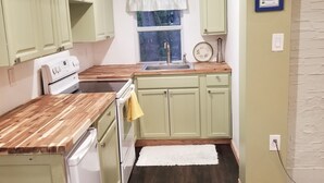 Eine kompakte Küche mit hellgrünen Schränken, einer Holz Arbeitsplatte, einem weißen Kühlschrank und einem Fenster mit Aussicht.