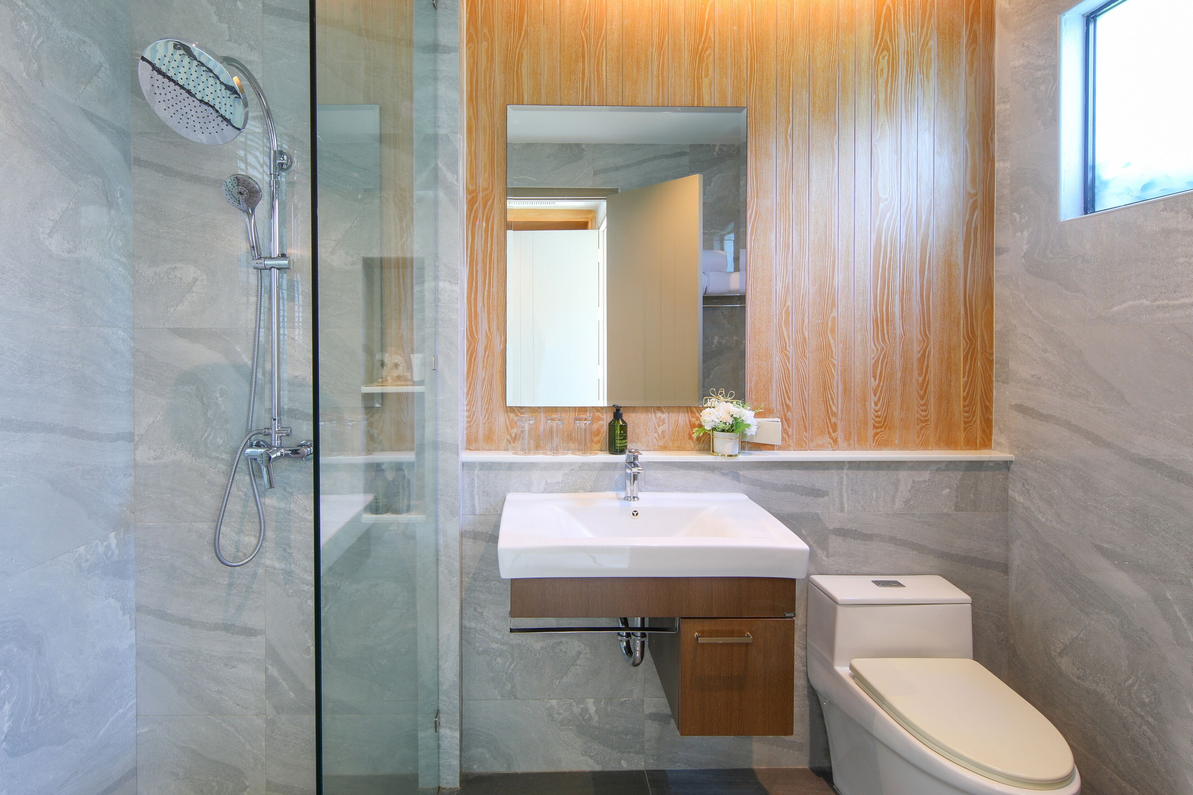 A modern bathroom with a glass shower enclosure, a wooden vanity, and a white toilet.