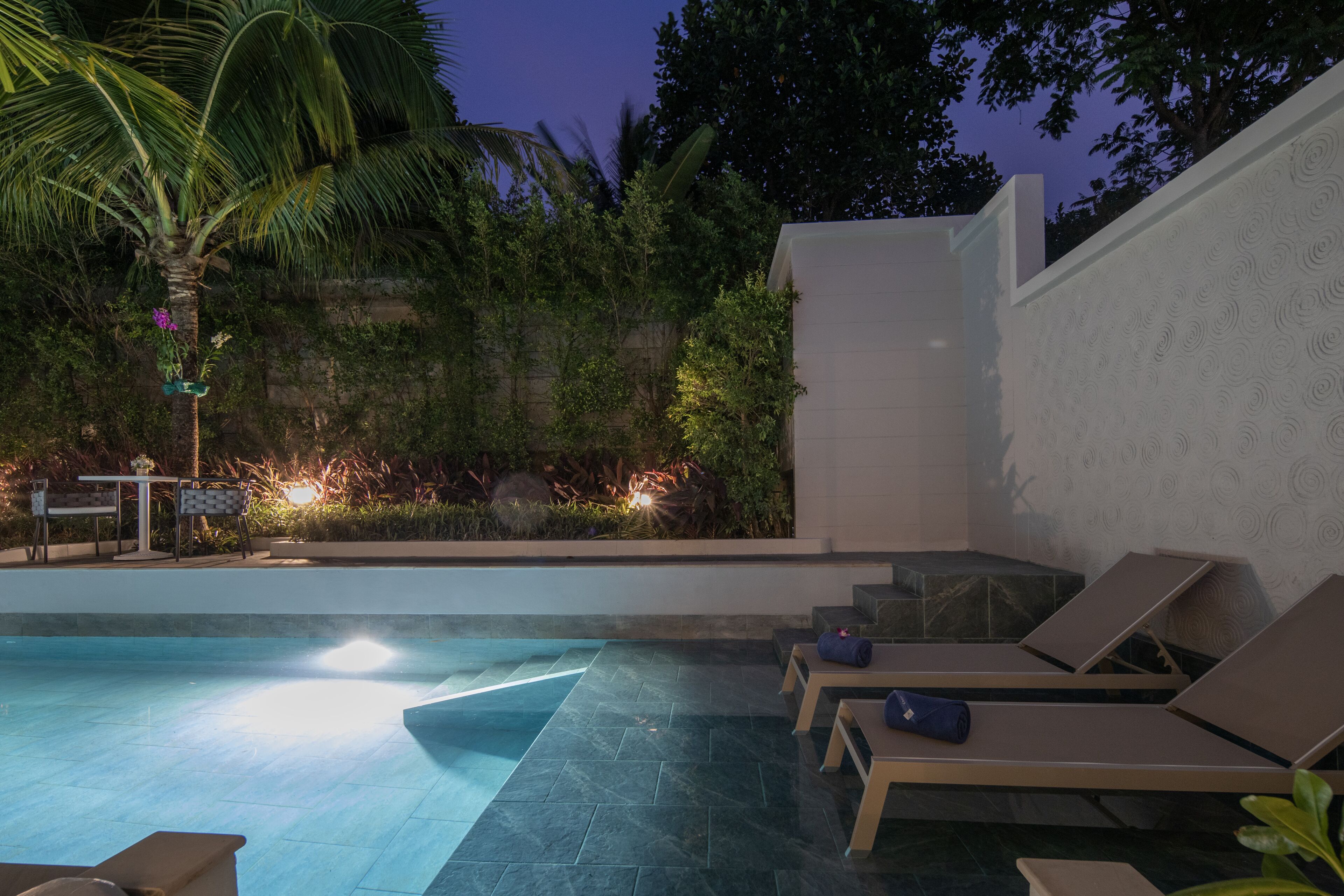 A pool area with lounge chairs, a small table, and a staircase leading to a covered area.