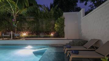 A pool area with lounge chairs, a small table, and a staircase leading to a covered area.