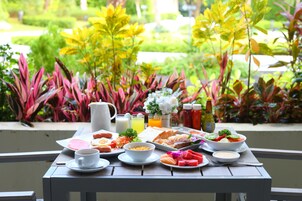 Una mesa dispuesta para el desayuno, con huevos, tostadas y fruta, y una vista de vegetación exuberante al fondo.