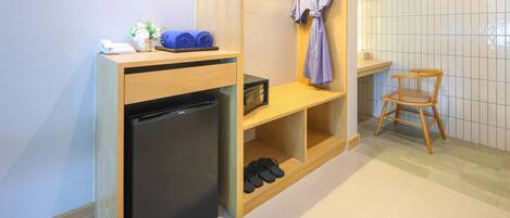 A compact kitchenette with a refrigerator, a microwave, and a shelf with rolled towels and a phone.