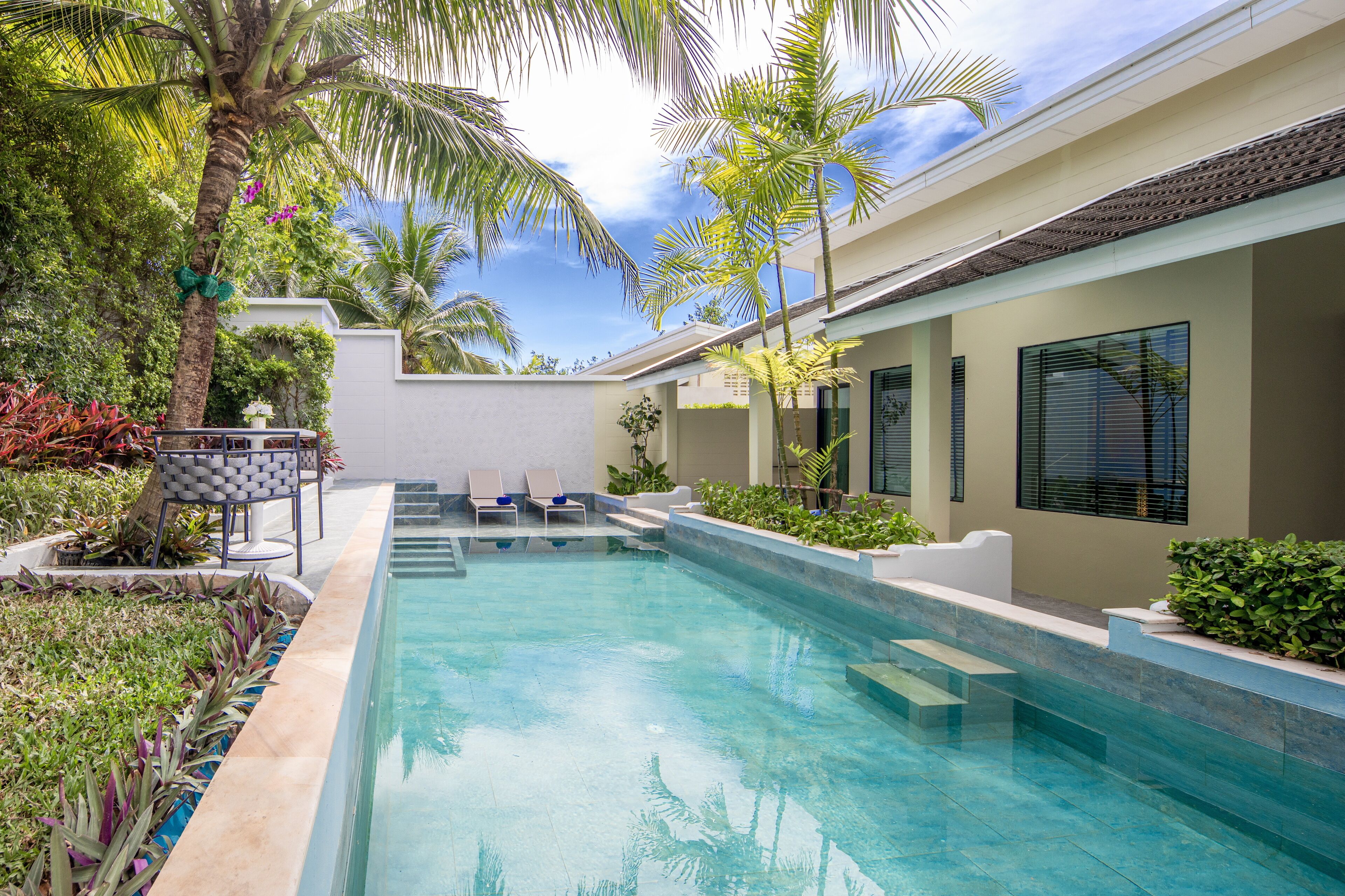 A swimming pool with lounge chairs and palm trees, surrounded by a well-maintained garden and a building with large windows.
