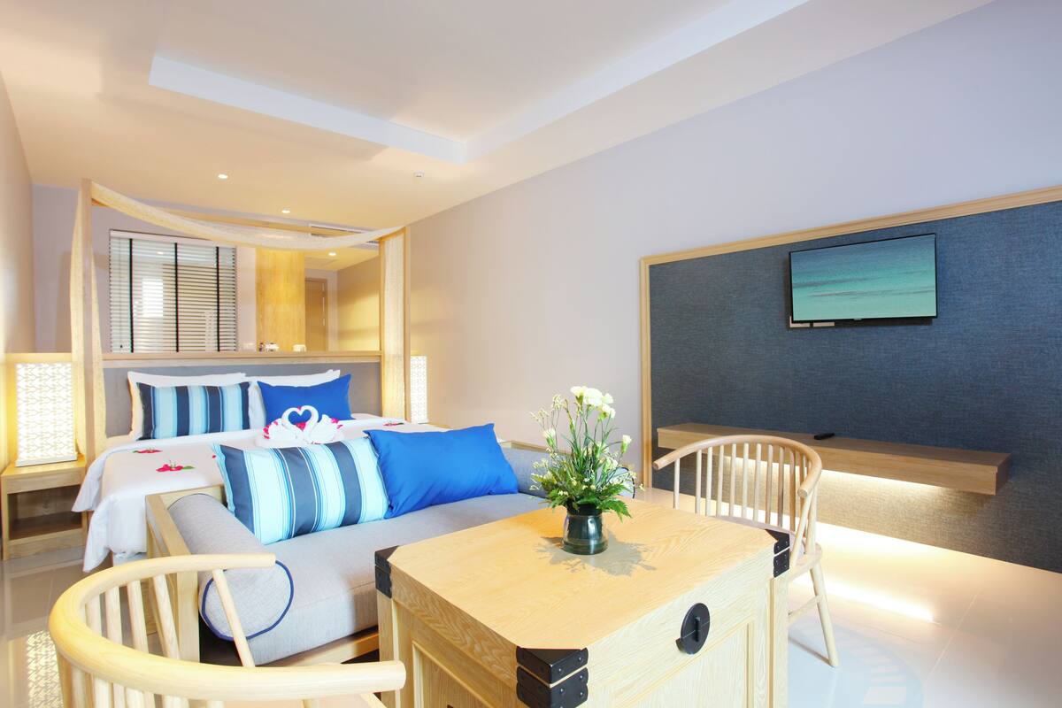 A hotel room with a bed, a sofa, a dining table, and a TV mounted on the wall.