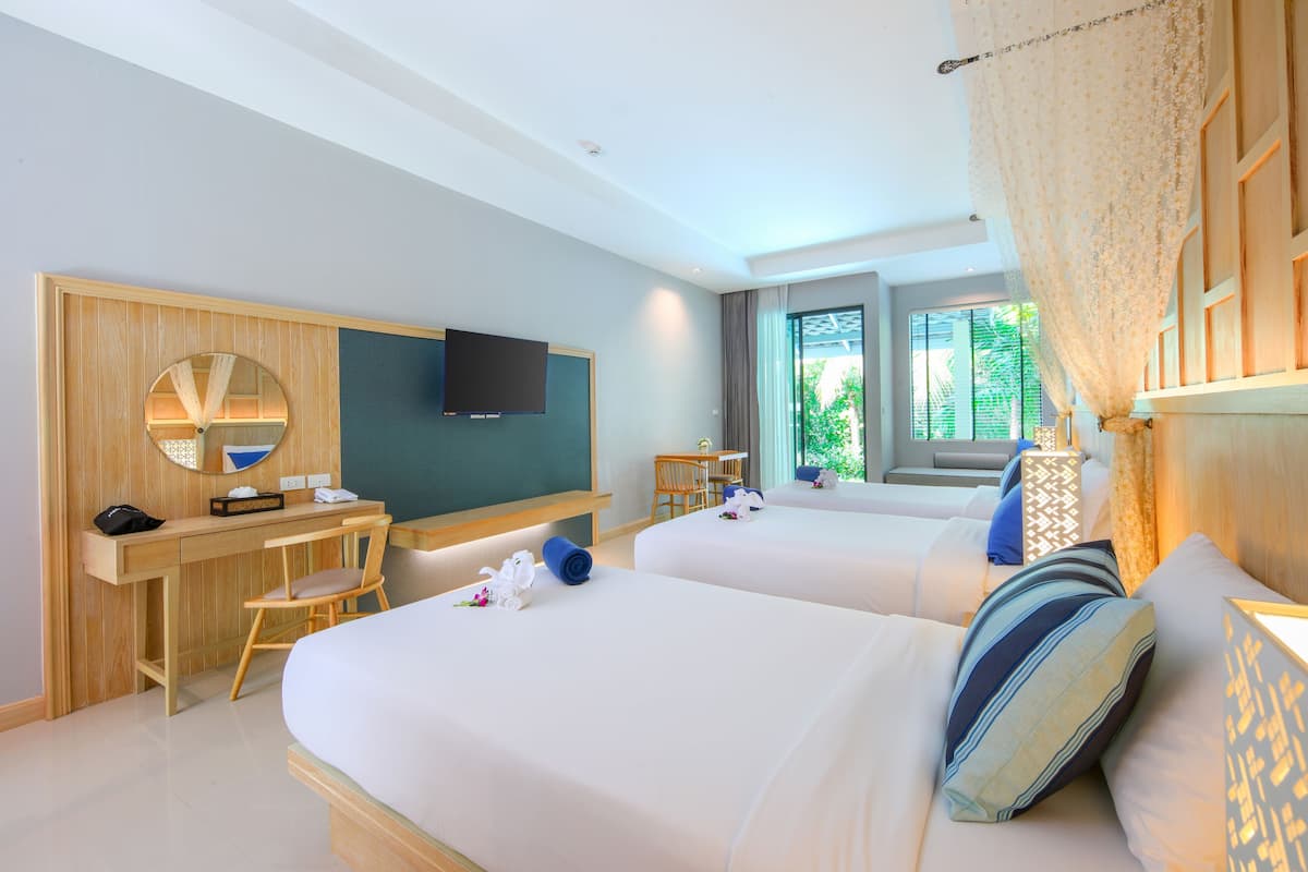 A hotel room with two beds, a desk with a chair, a TV, and a window with a view of greenery.