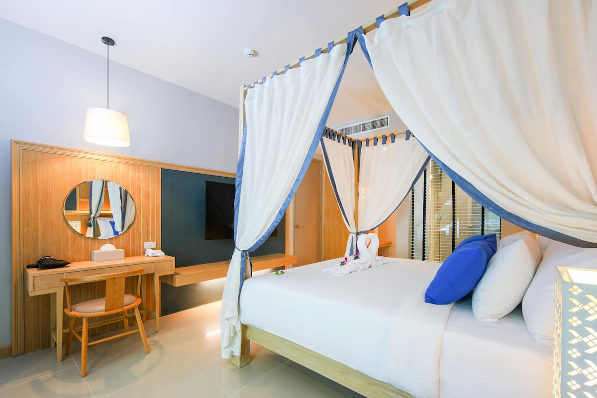 A hotel room with a bed, a desk, a chair, a mirror, and a window with blinds.