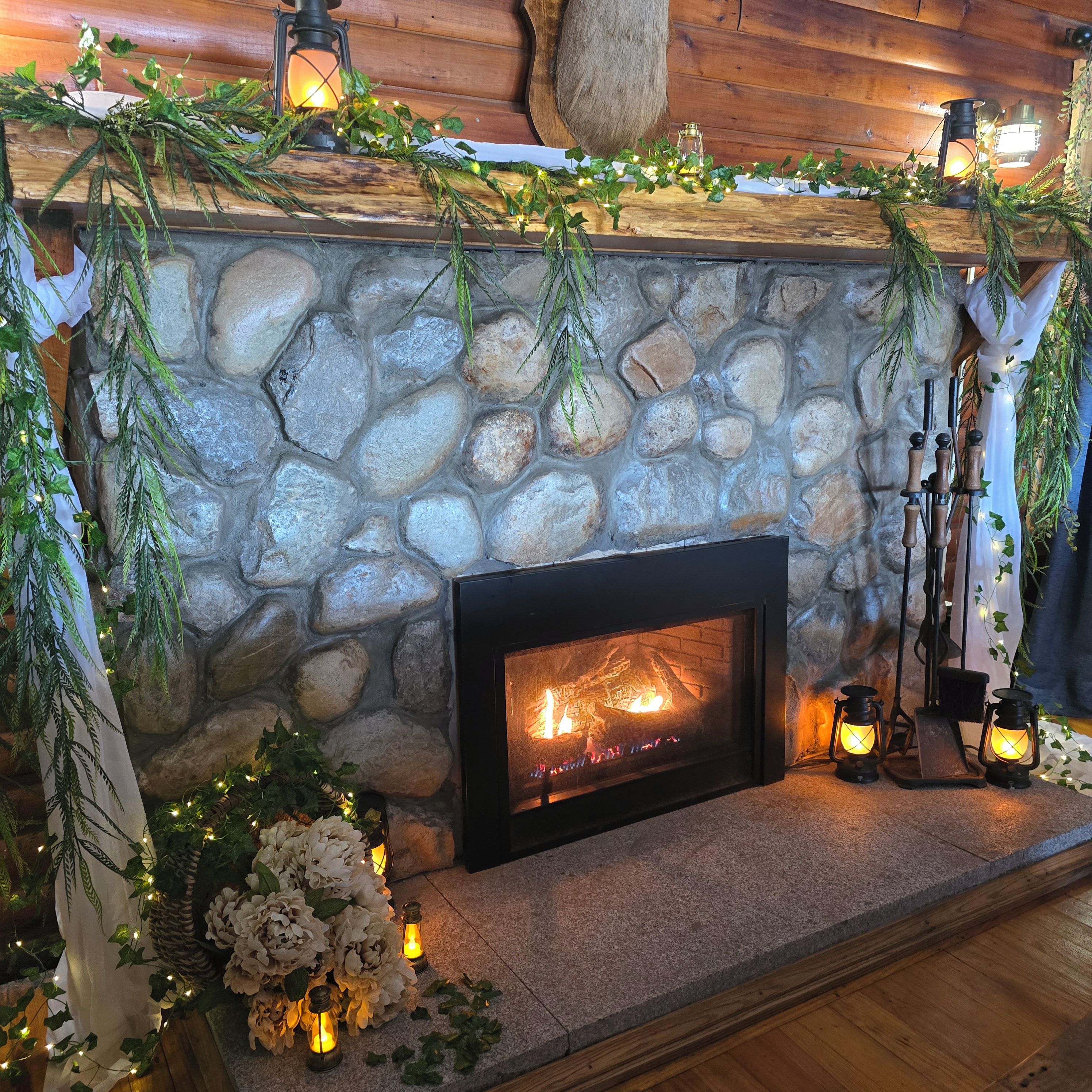 A stone fireplace with a fire, surrounded by greenery and candles.
