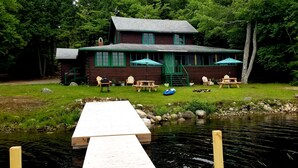 Une cabane en rondins avec un quai s’avançant dans un lac paisible, le tout entouré d’une végétation luxuriante.
