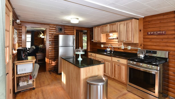 Une cuisine rustique aménagée dans une cabane en rondins, avec des meubles en bois, un réfrigérateur en acier inoxydable, une cuisinière et une machine à café.