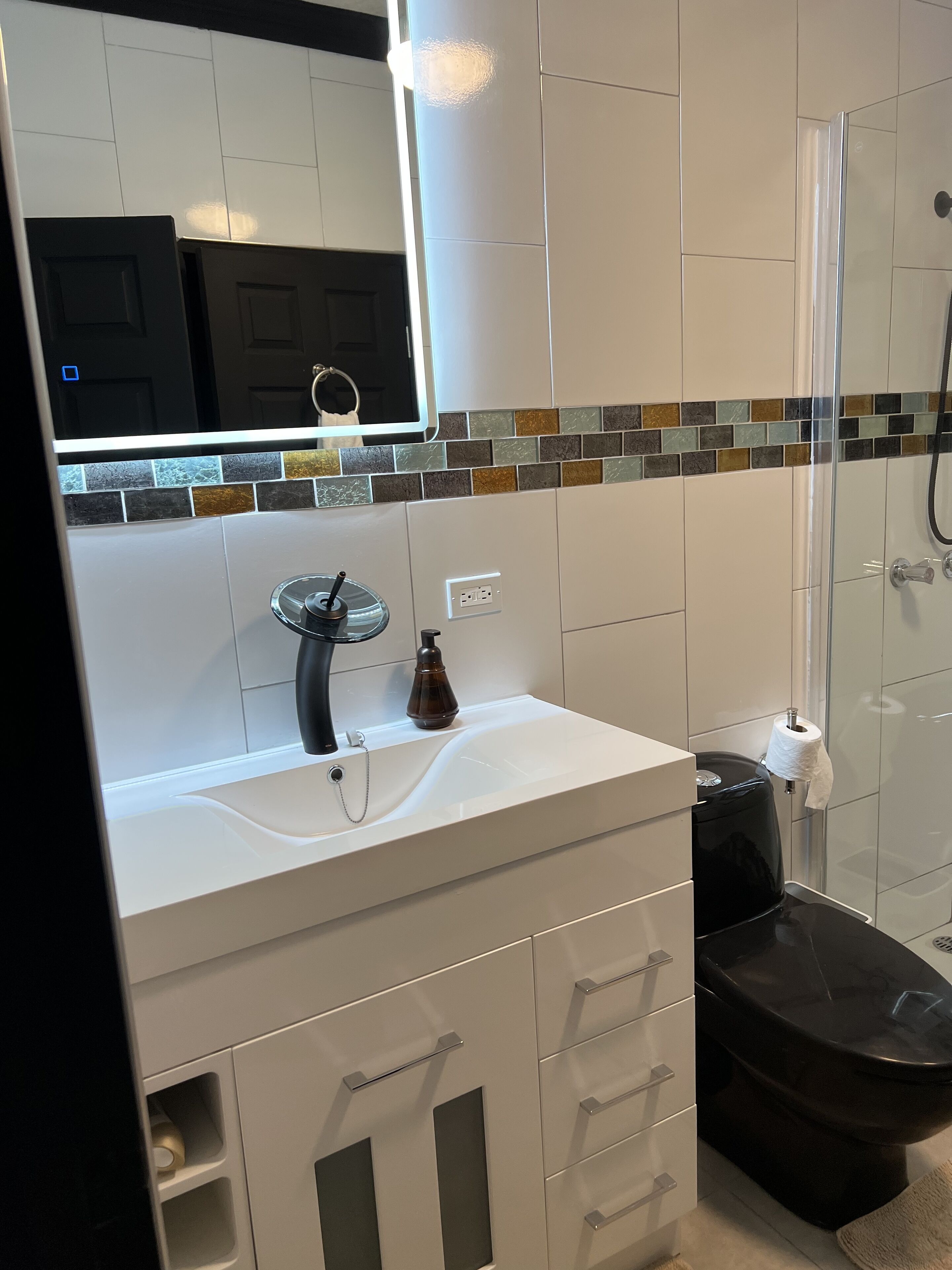 A modern bathroom with a white vanity, a black toilet, and a glass shower enclosure.