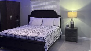 Une chambre à coucher comprenant un lit, un ventilateur de plafond, un climatiseur, une table de chevet avec une lampe et une armoire.