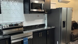 Une cuisine moderne dotée d’appareils électroménagers en acier inoxydable, de meubles de rangement noirs et d’un four à micro-ondes encastré.